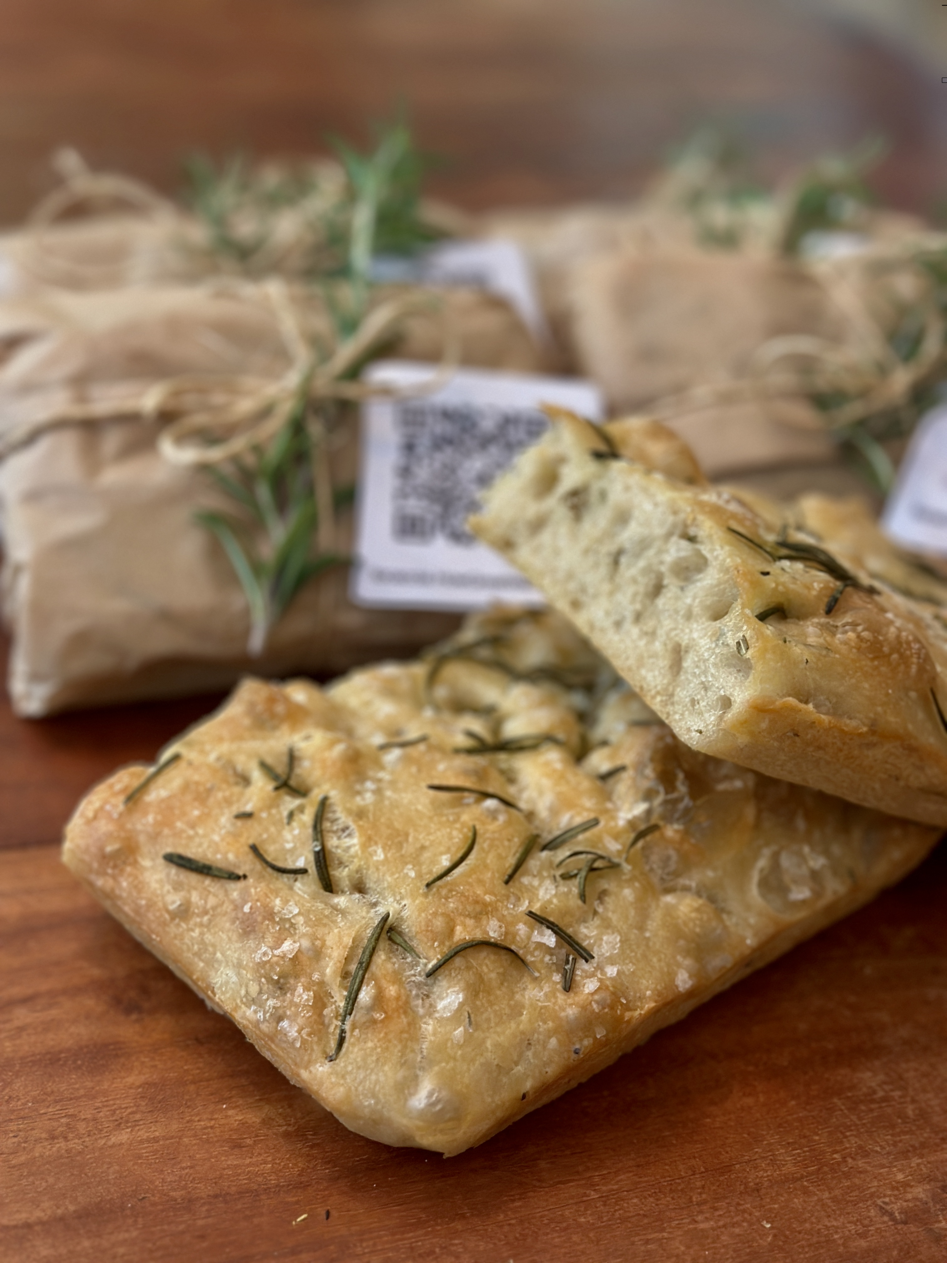 Sliced focaccia with rosemary, wrapped loaves in the background